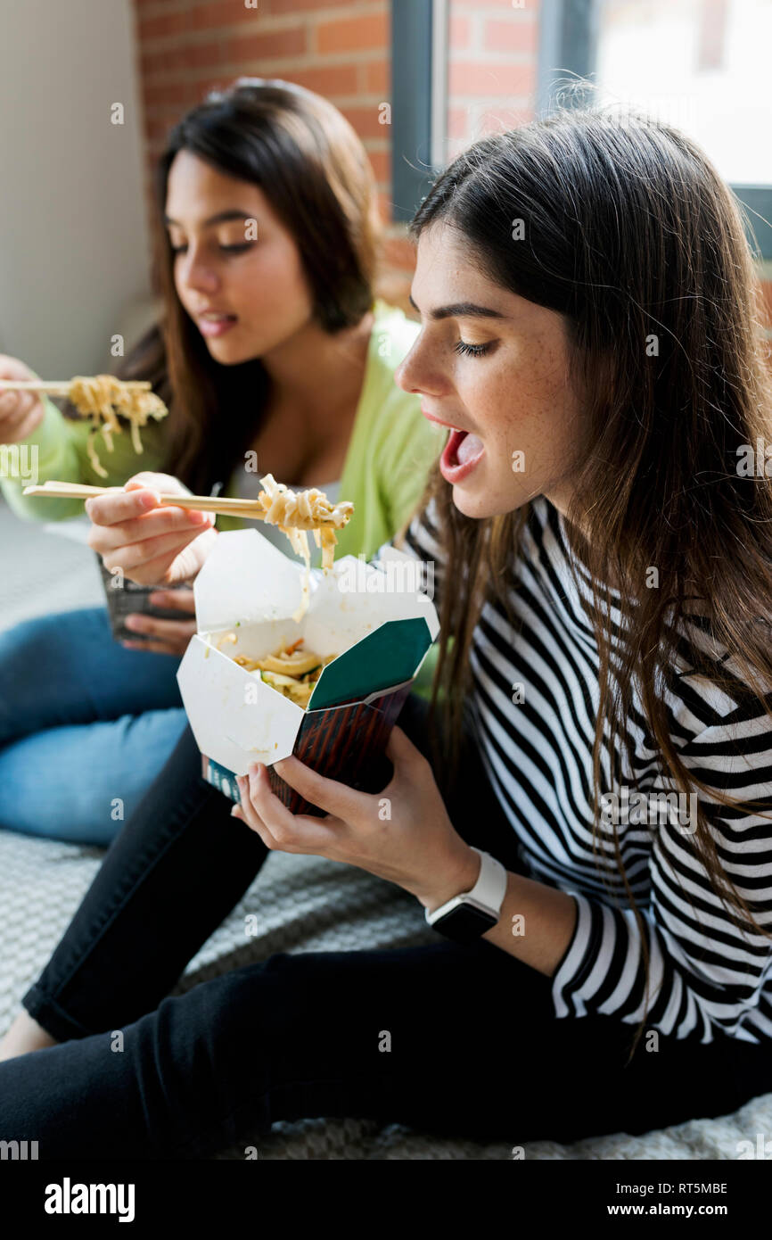 Two young women having Asian takeaway food at home Stock Photo