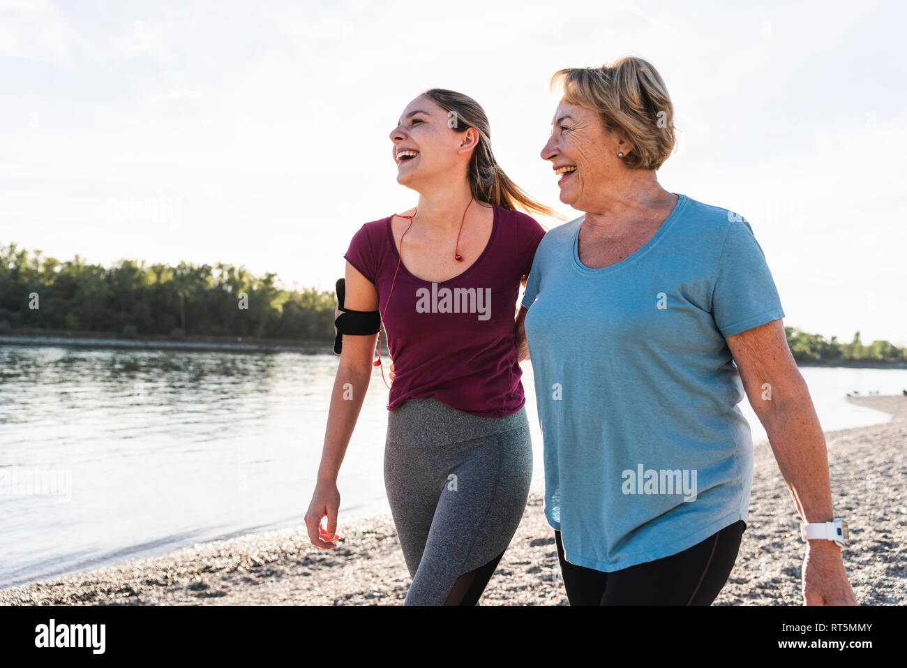 Fit grandmother and granddaughter walking at the river with arms around, having fun Stock Photo