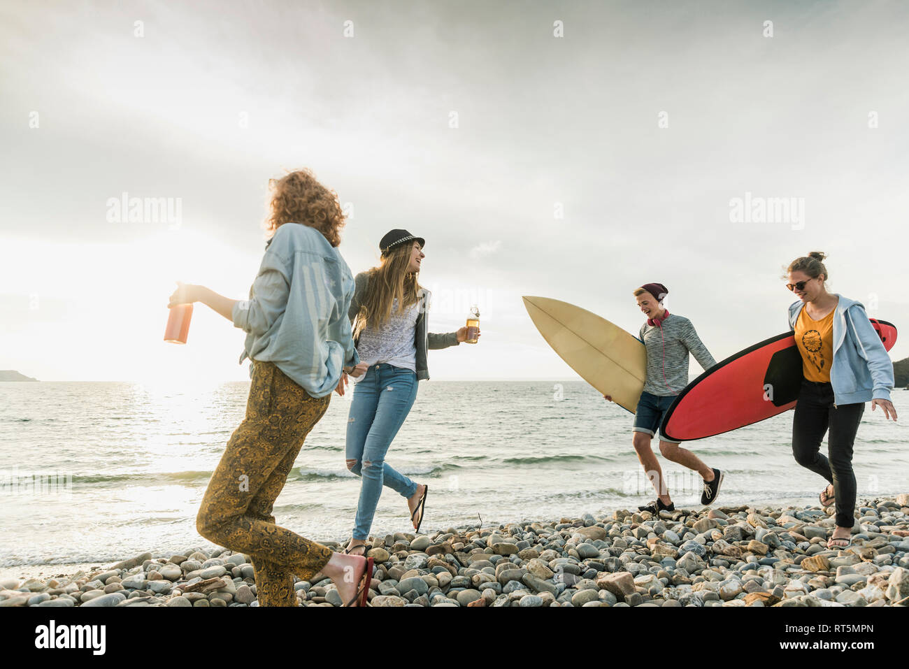 Happy friends with surfboards walking on stony beach Stock Photo