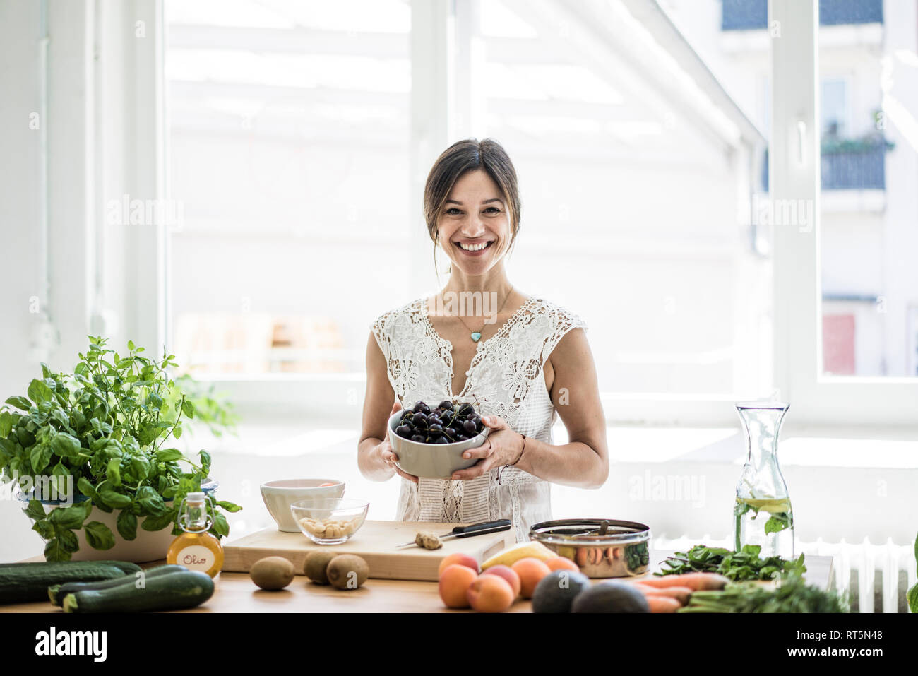 Woman preparing healthy food in her kitchen, holding bowl of cherries Stock Photo