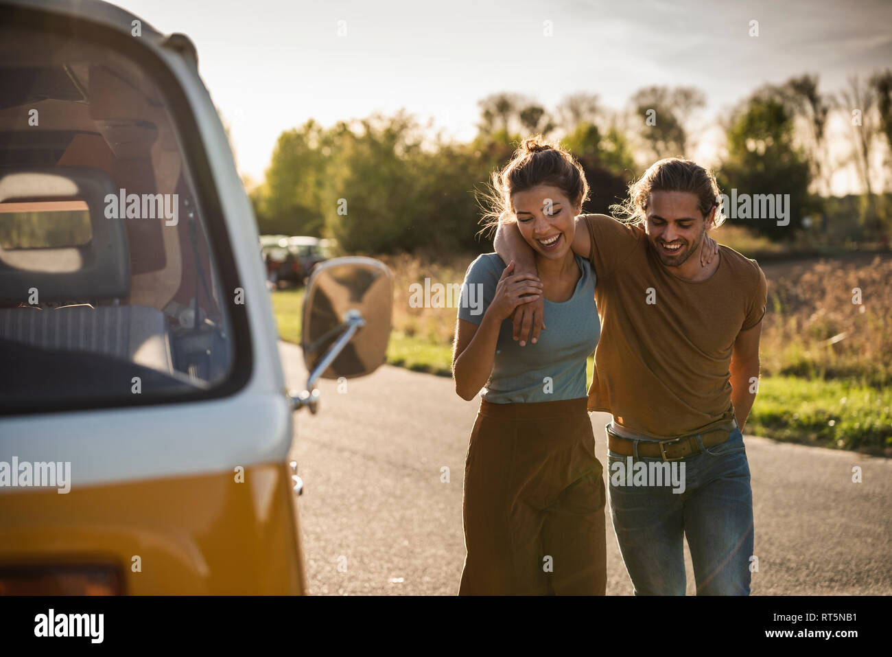 Affectionate couple walking on the road with arms around, next to their camper Stock Photo