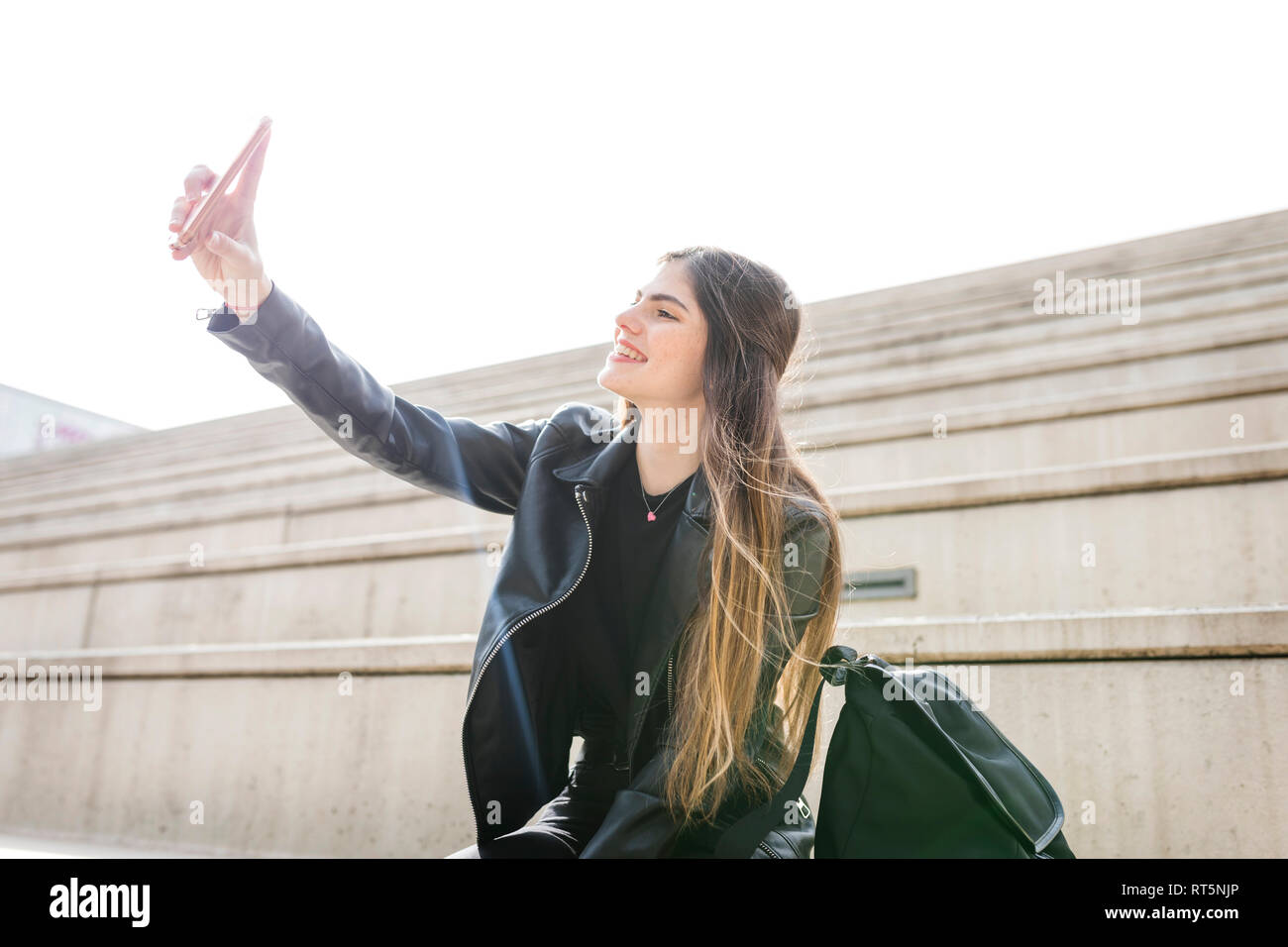 Smiling young woman sitting on stairs taking a selfie Stock Photo