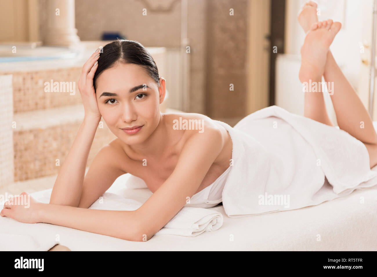 Beautiful Asian Woman In Towel Lying On Massage Table And Looking At