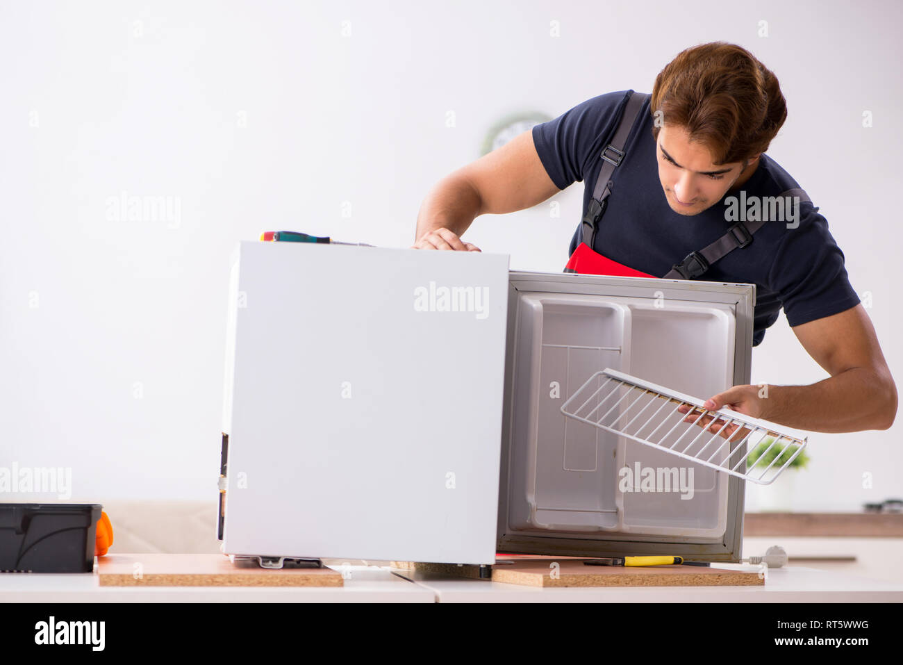 Young handsome contractor repairing fridge Stock Photo