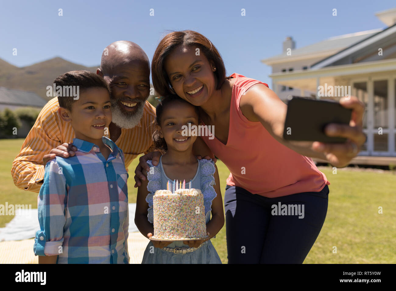 Multi-generation family taking selfie with mobile phone while celebrating birthday of grandaughter Stock Photo