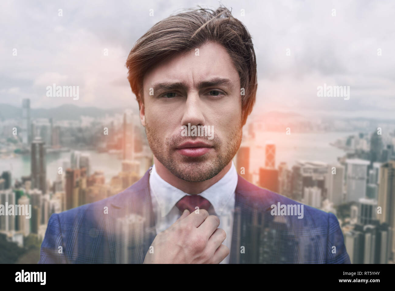 Totally handsome. Close-up portrait of handsome young businessman adjusting his necktie while standing against of cityscape background. Business style. Fashion look. Business concept. Stock Photo