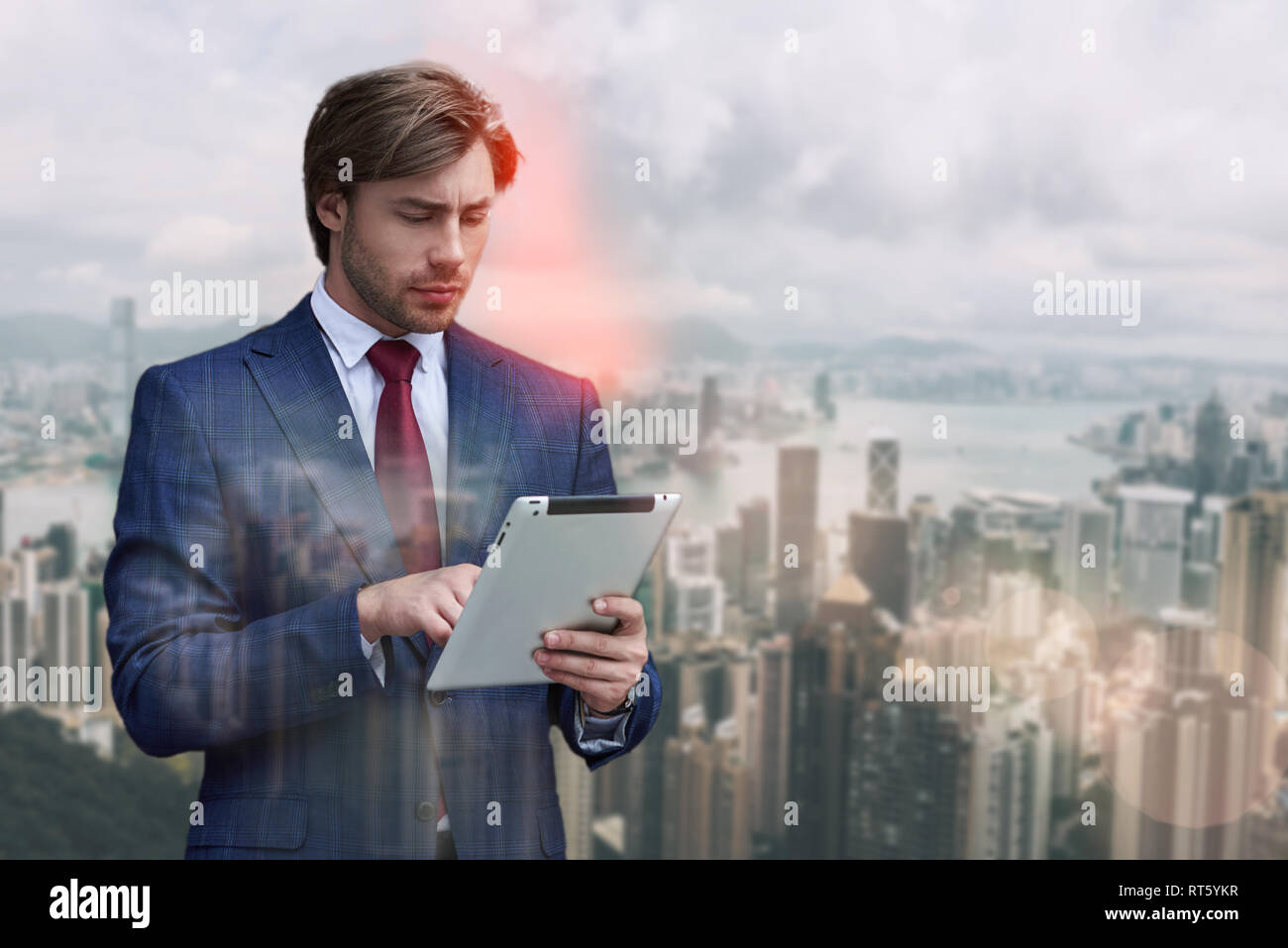 Checking his mail. Handsome bearded businessman in suit using digital tablet while standing against of cityscape background. IT specialist. Digital concept Stock Photo