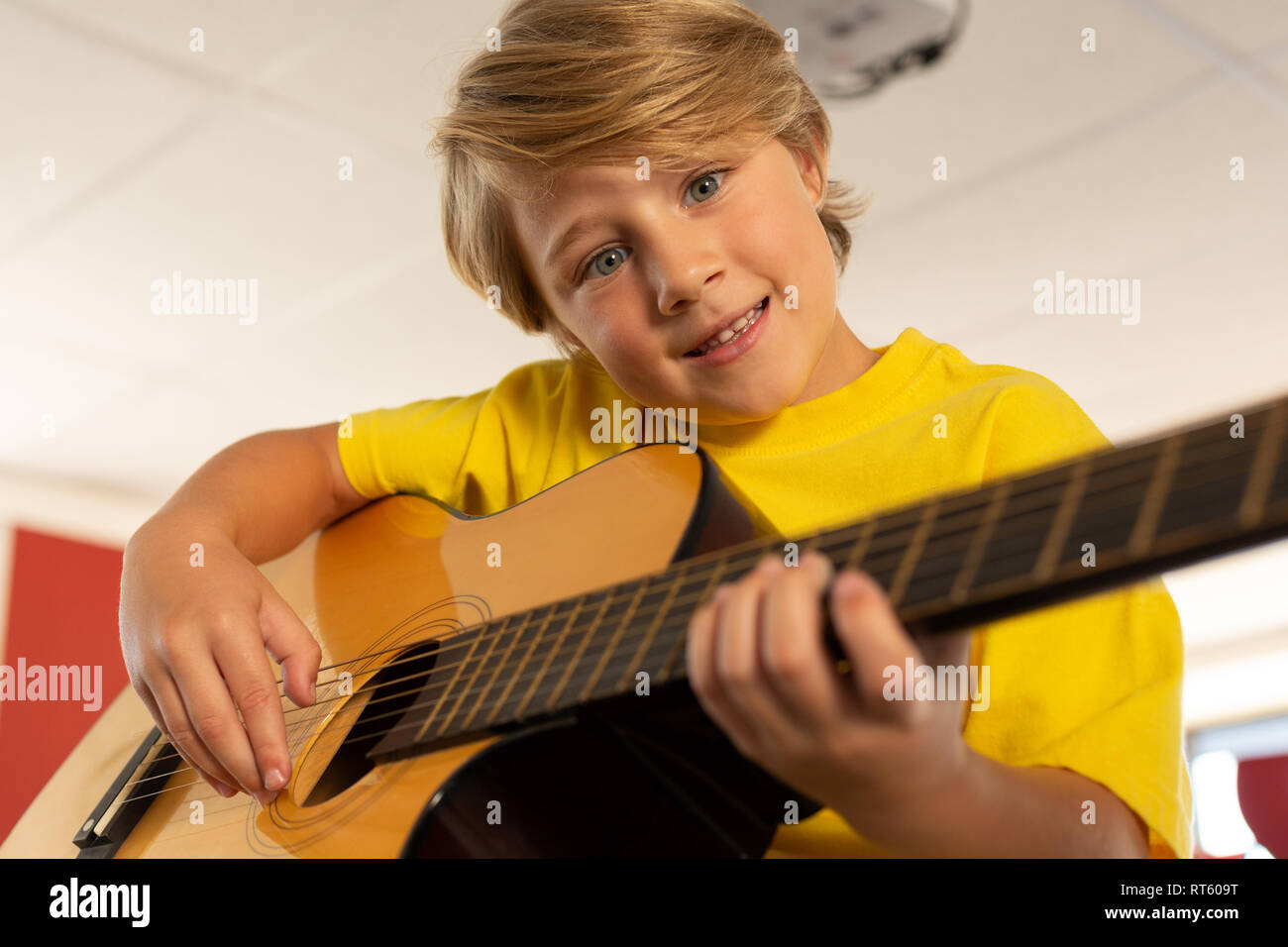 Boy looking at camera while playing guitar in a classroom Stock Photo