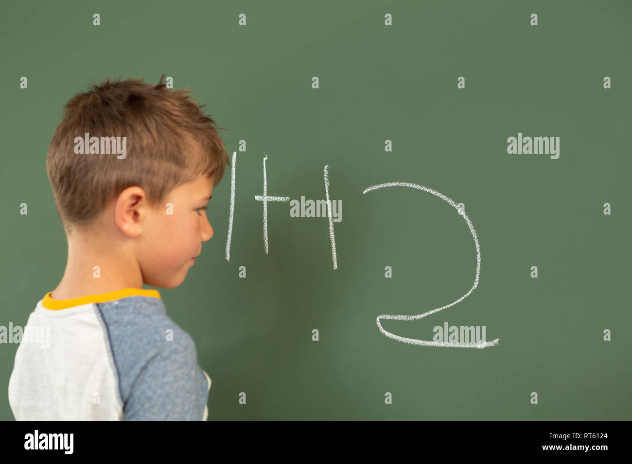 Schoolboy doing math on green chalkboard in a classroom Stock Photo