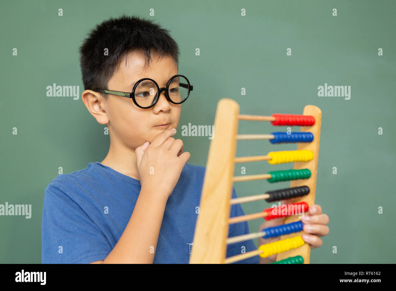 Thoughtful boy learning math with abacus against green chalkboard in a classroom Stock Photo