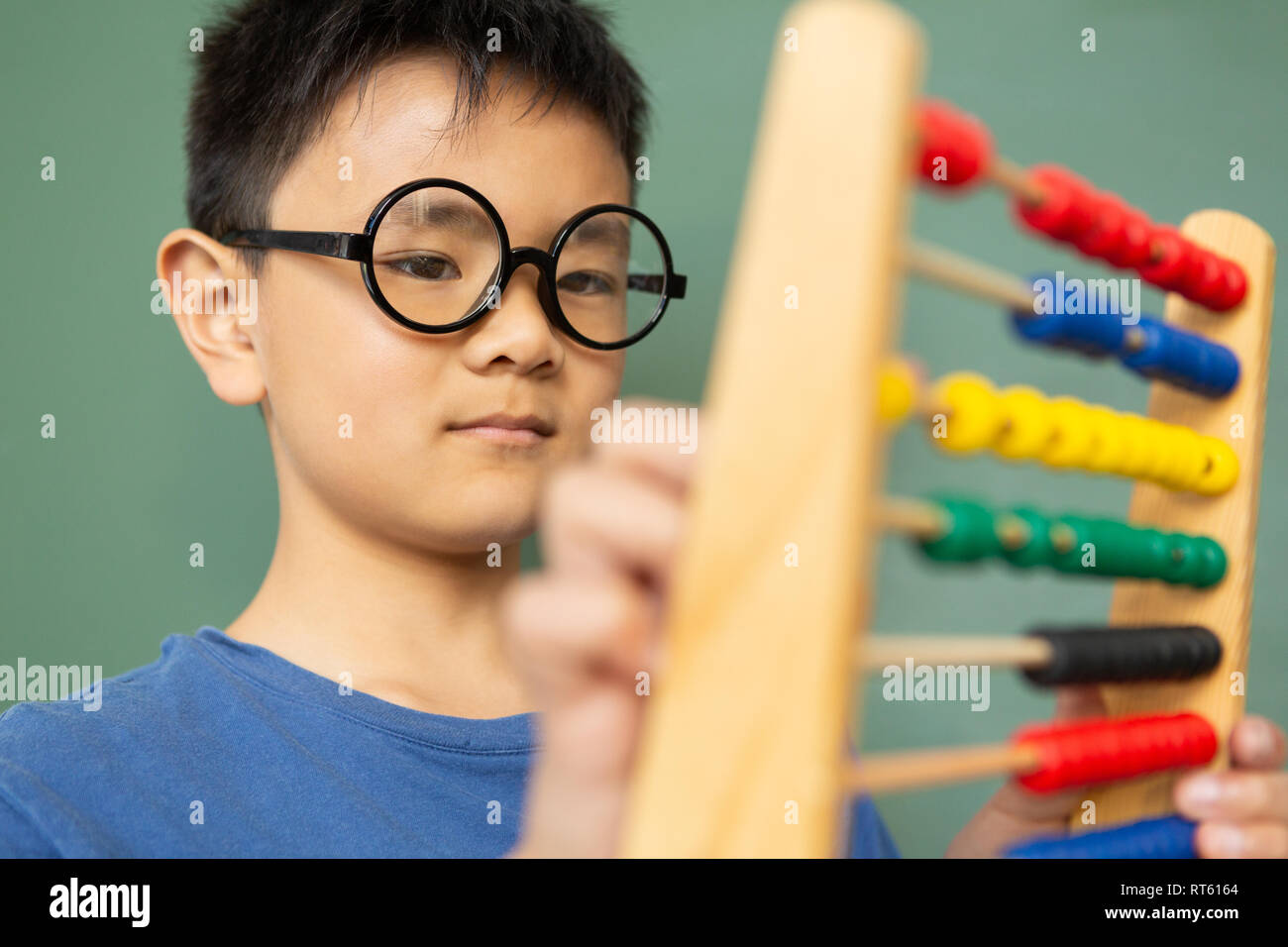 Boy learning math with abacus against green chalkboard in a classroom Stock Photo