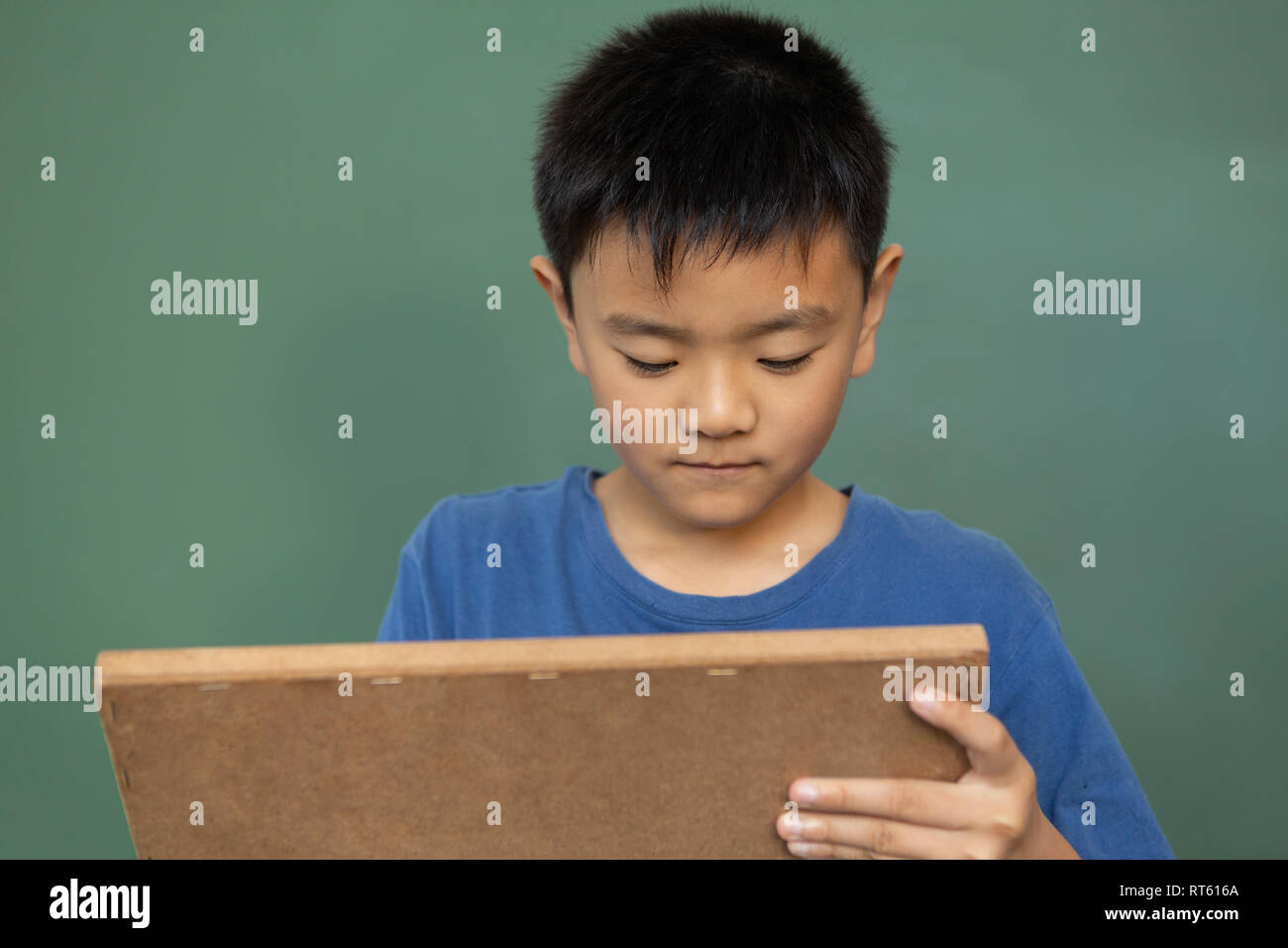 Schoolboy writing on chalk slate against green chalkboard in a classroom Stock Photo