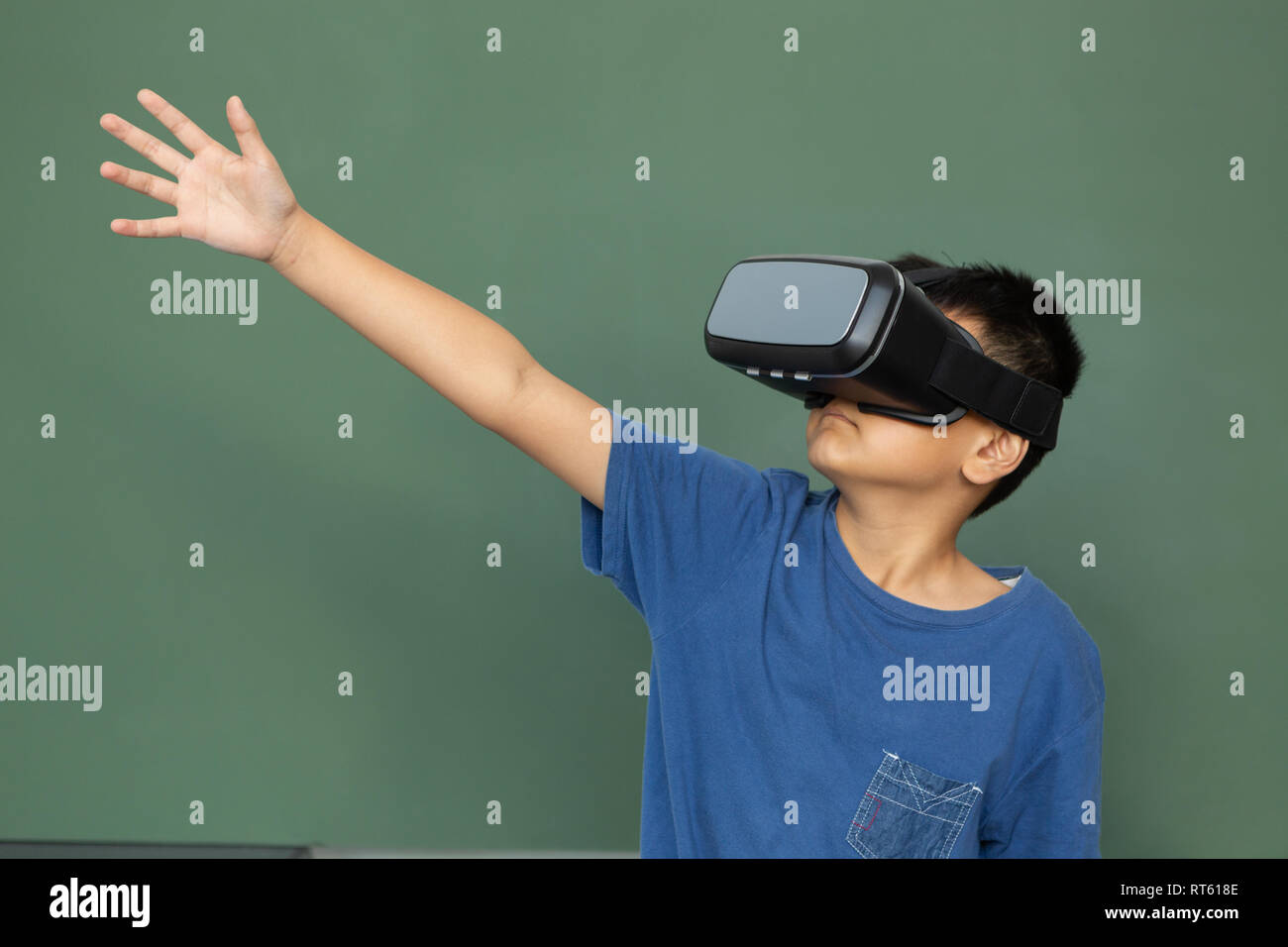 Schoolboy using virtual reality headset against greenboard in a classroom Stock Photo