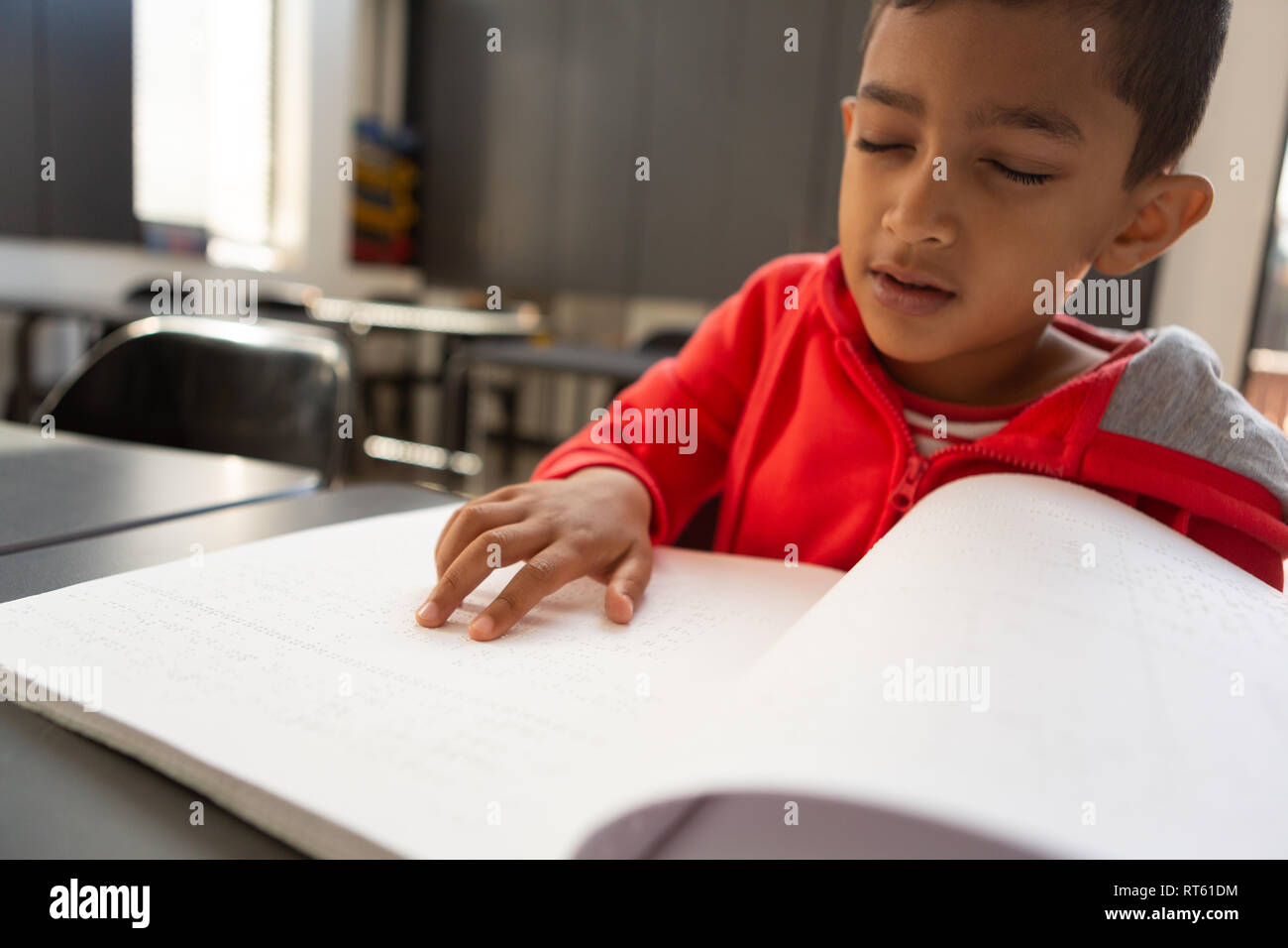 Blind schoolboy reading a braille book at desk in a classroom Stock Photo