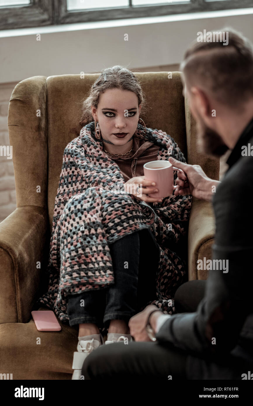 Smoky eyes. Dark-eyed teenage girl with smoky eyes taking cup of tea from professional counselor Stock Photo