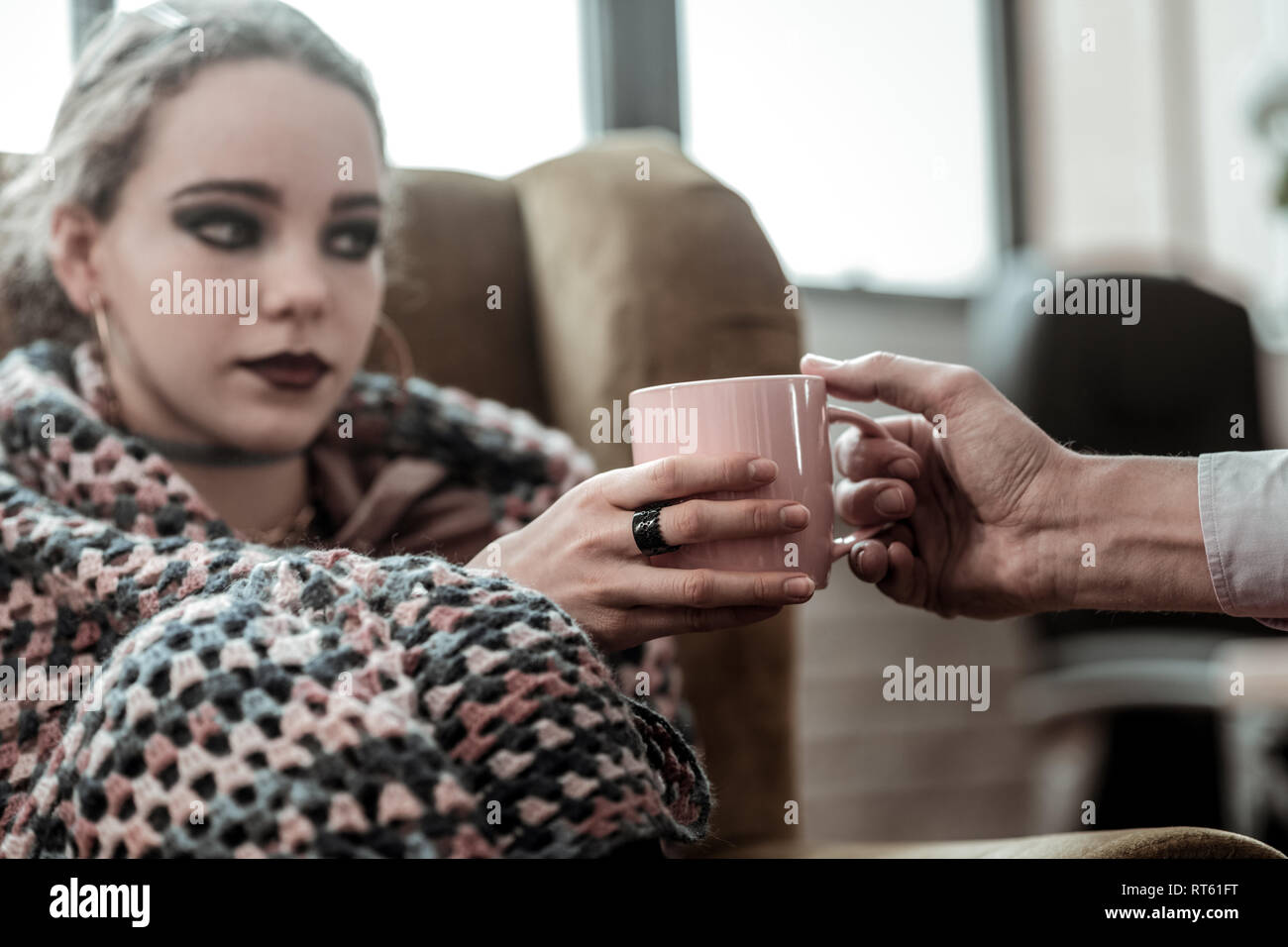 Pink cup. Teenage daughter with smoky eyes taking pink cup of tea from caring father Stock Photo