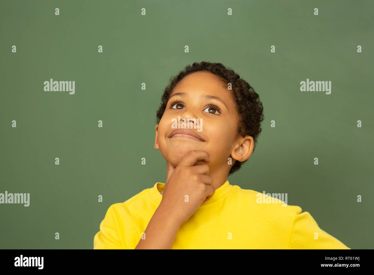 Thoughtful schoolboy standing against greenboard in a classroom Stock Photo