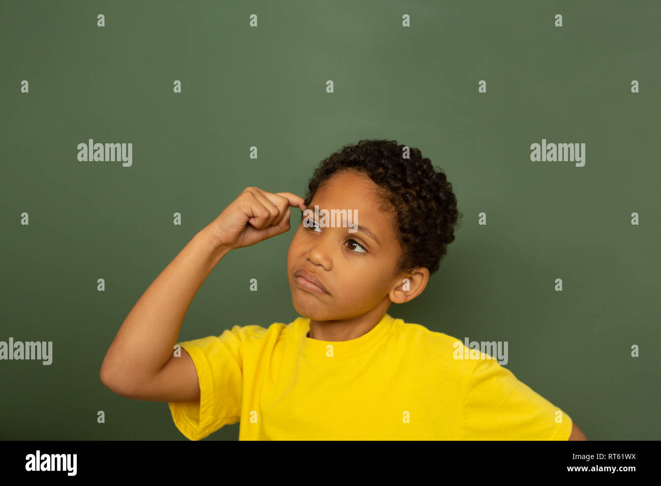 Thoughtful schoolboy with finger pointing to head standing against greenboard Stock Photo
