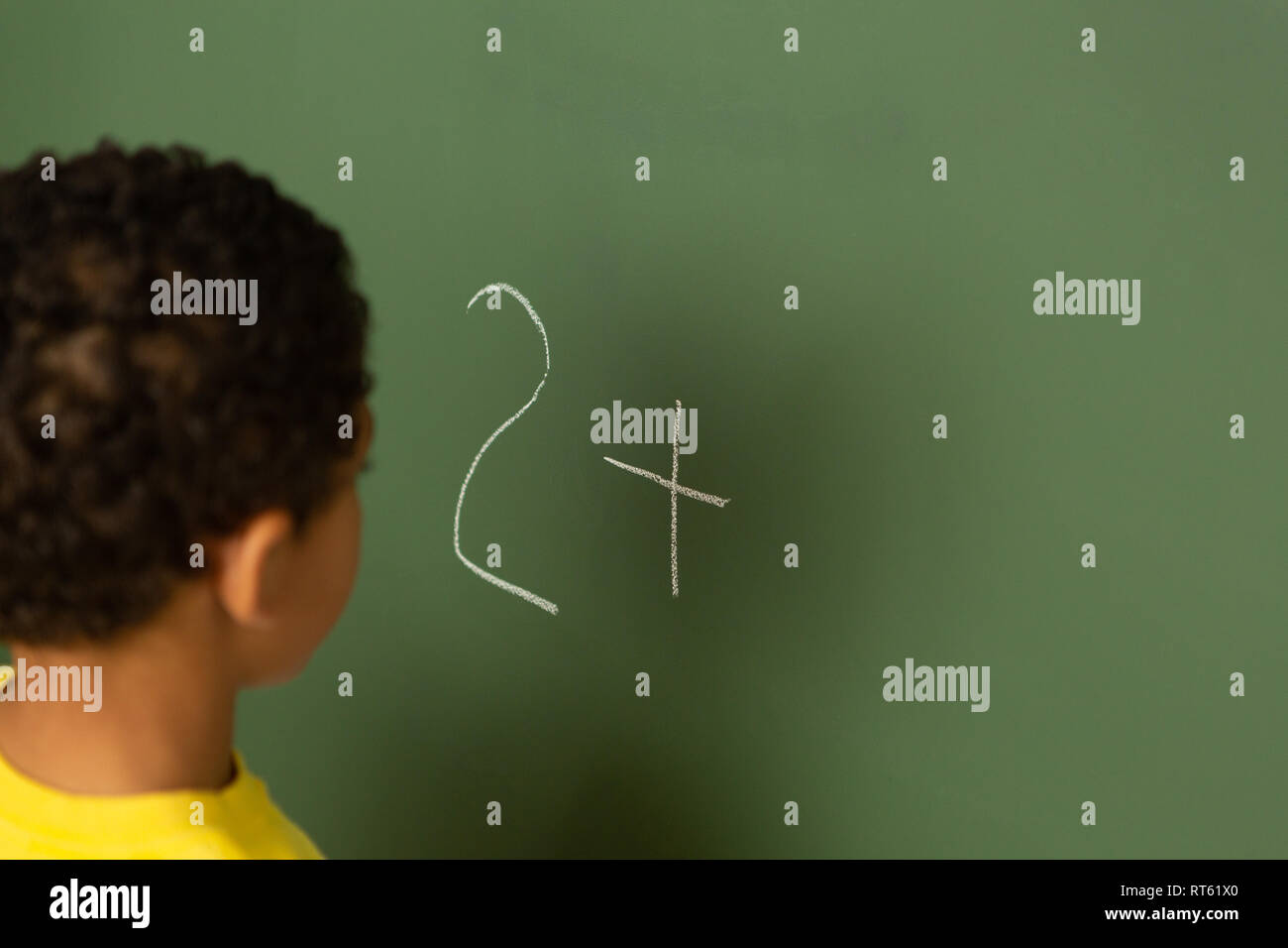 Schoolboy doing math on greenboard in a classroom Stock Photo