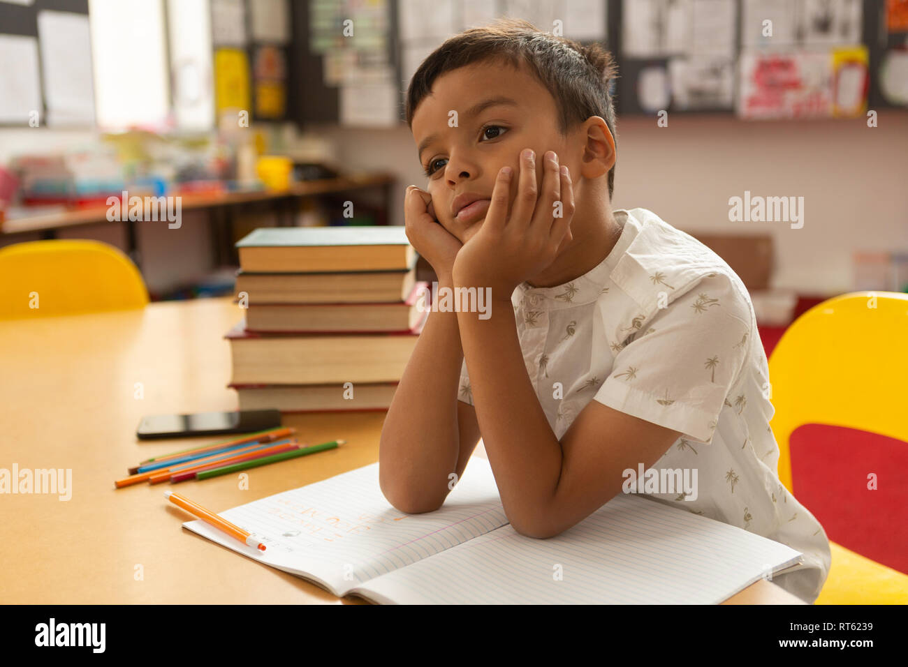 Thoughtful schoolboy studying at desk in a classroom Stock Photo - Alamy