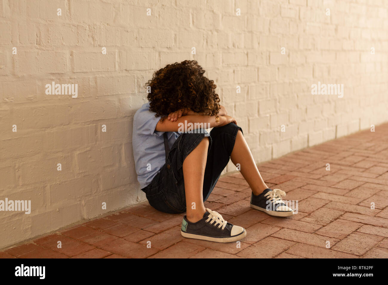 Sad schoolgirl sitting alone on floor in the corridor Stock Photo