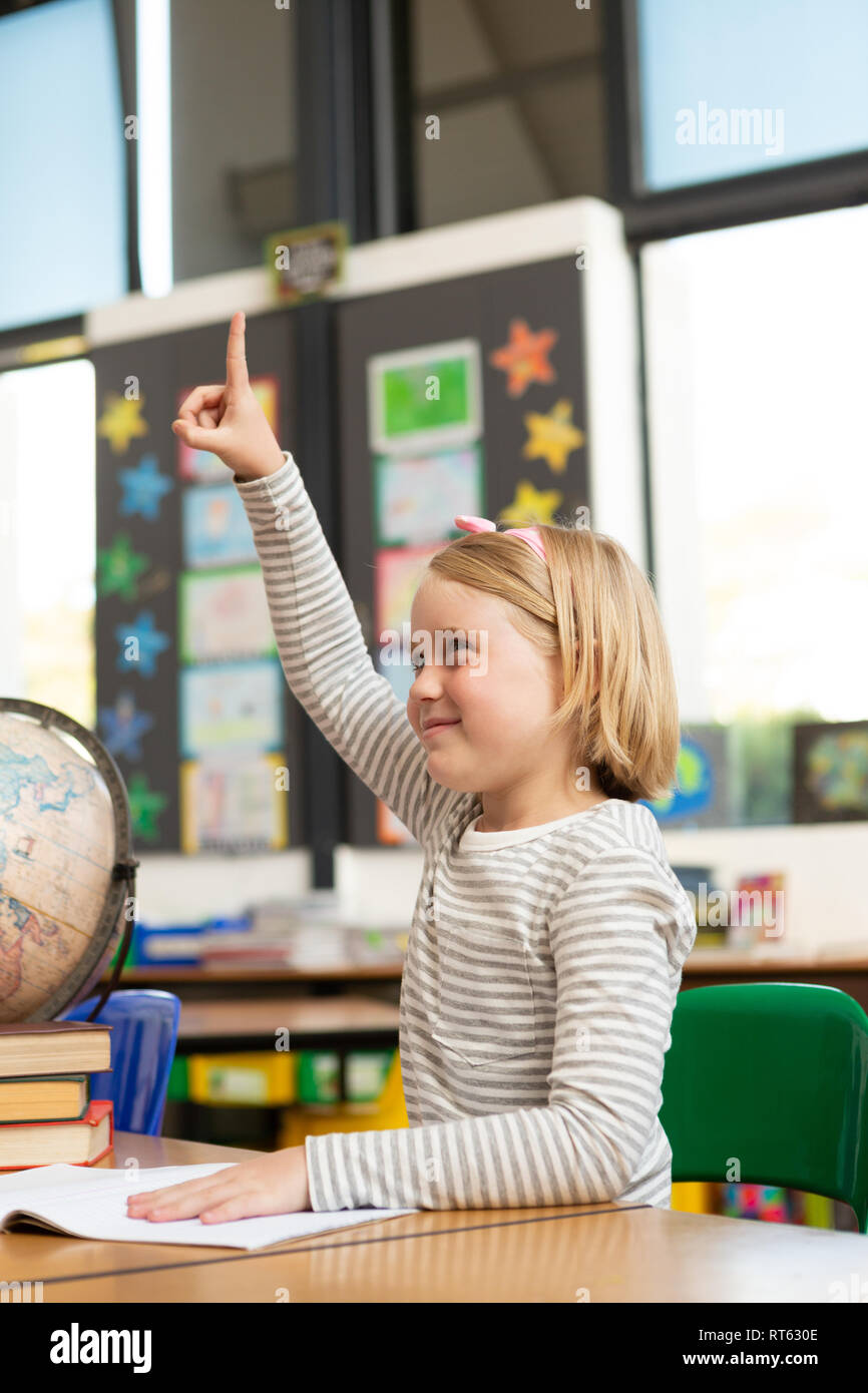 Schoolgirl raising her hand at desk in the classroom Stock Photo - Alamy