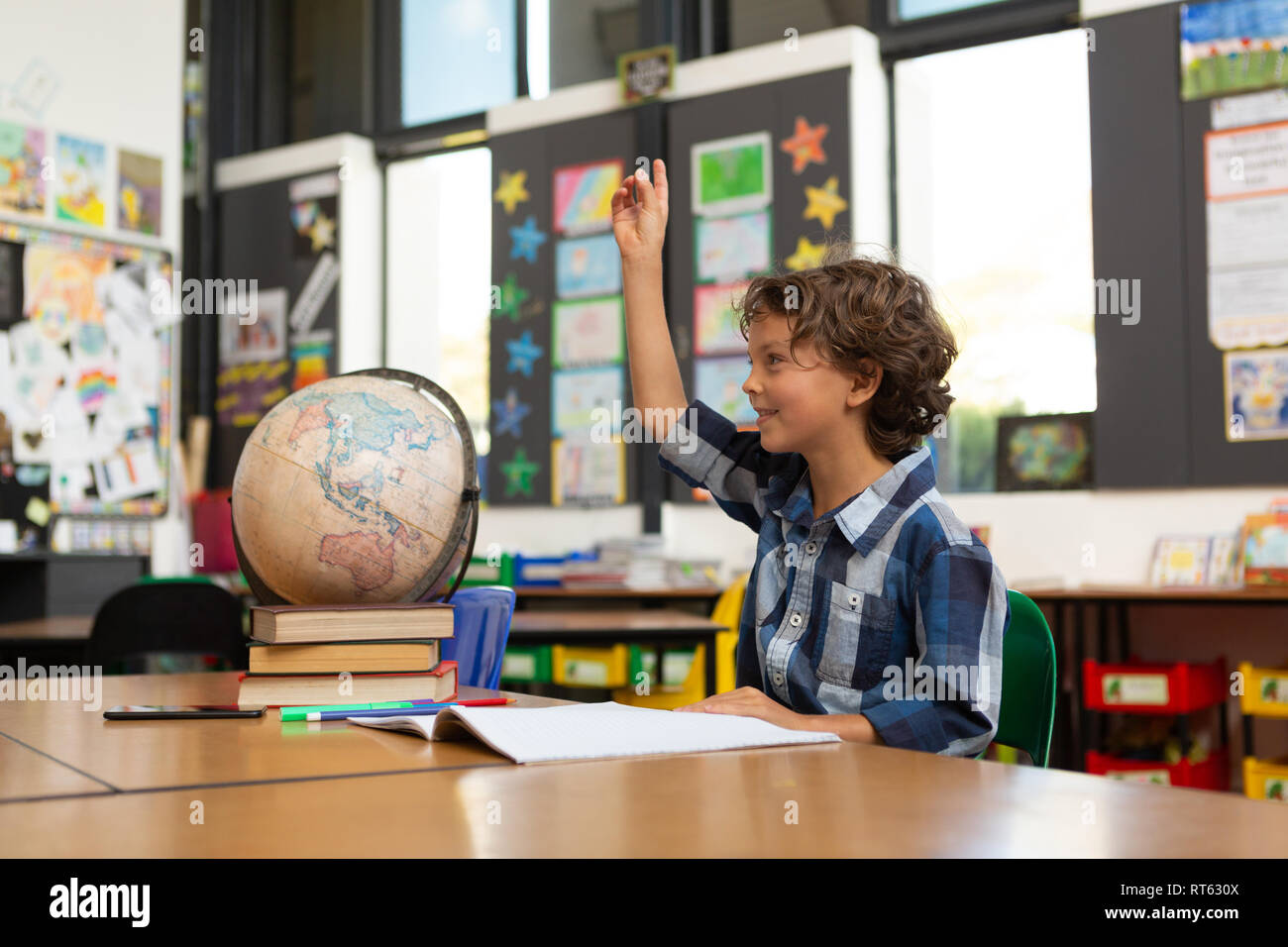 Schoolboy raising his hand at desk in the classroom Stock Photo - Alamy
