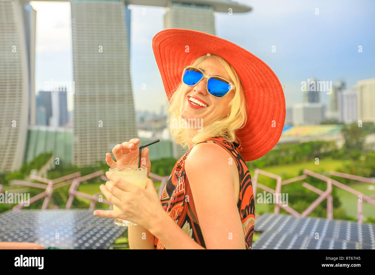 Travel holiday vacation in Singapore, Southeast Asia. Lifestyle caucasian woman with wide hat drinking aperitif at rooftop. Aerial view or cityscape Stock Photo