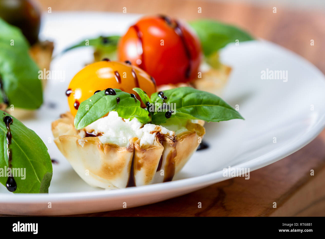 delicious puff pastry cups filled and baked with goat cheese topped with fresh basil and tomato with a balsamic drizzle Stock Photo