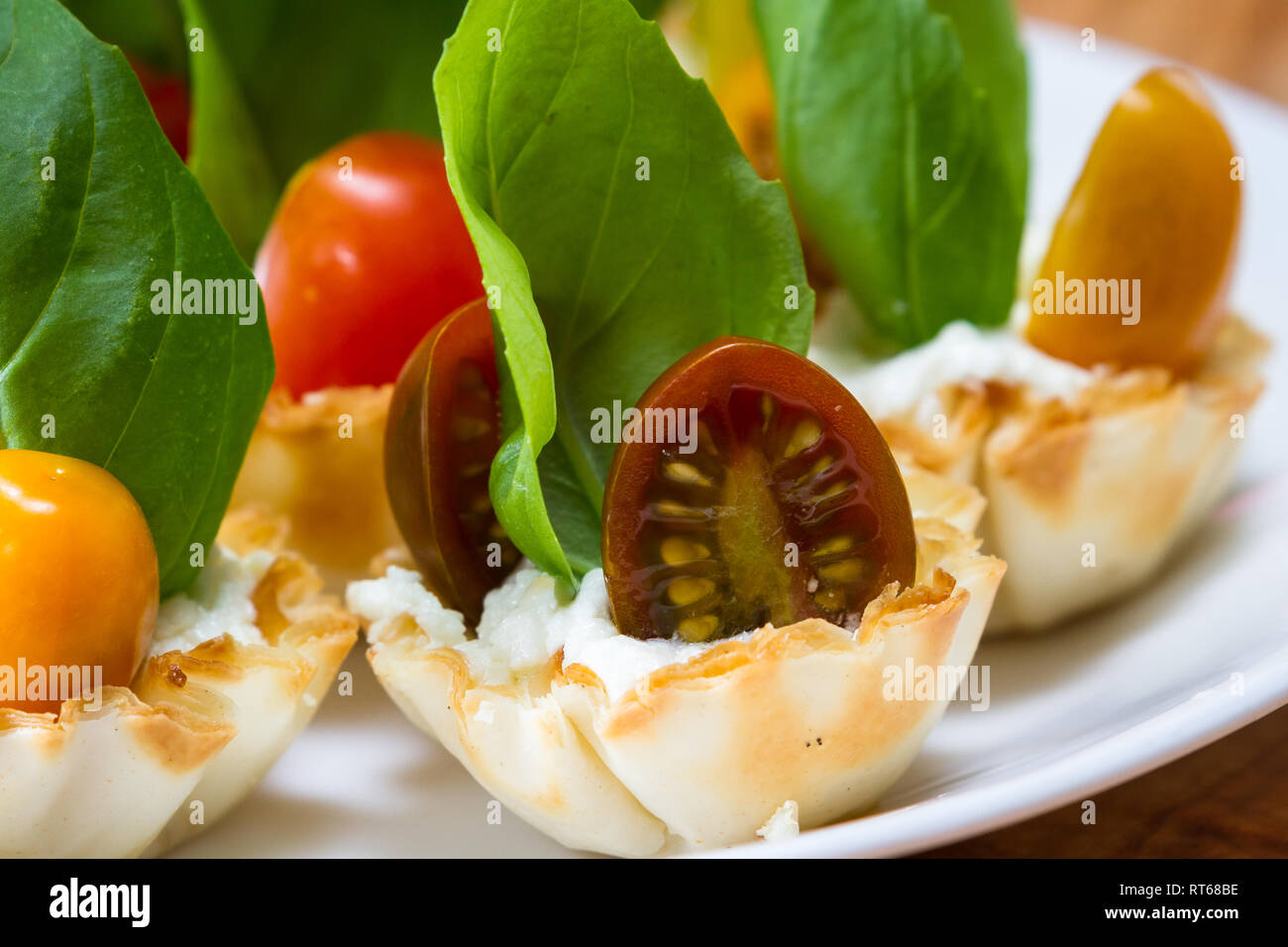 delicious puff pastry cups filled and baked with goat cheese topped with fresh basil and cherry tomato Stock Photo