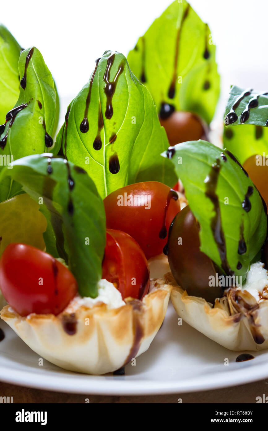 delicious puff pastry cups filled and baked with goat cheese topped with fresh basil and tomato with a balsamic drizzle Stock Photo