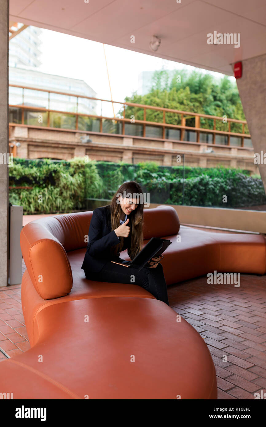 Smiling young businesswoman sitting in a lounge using tablet for a video conference Stock Photo