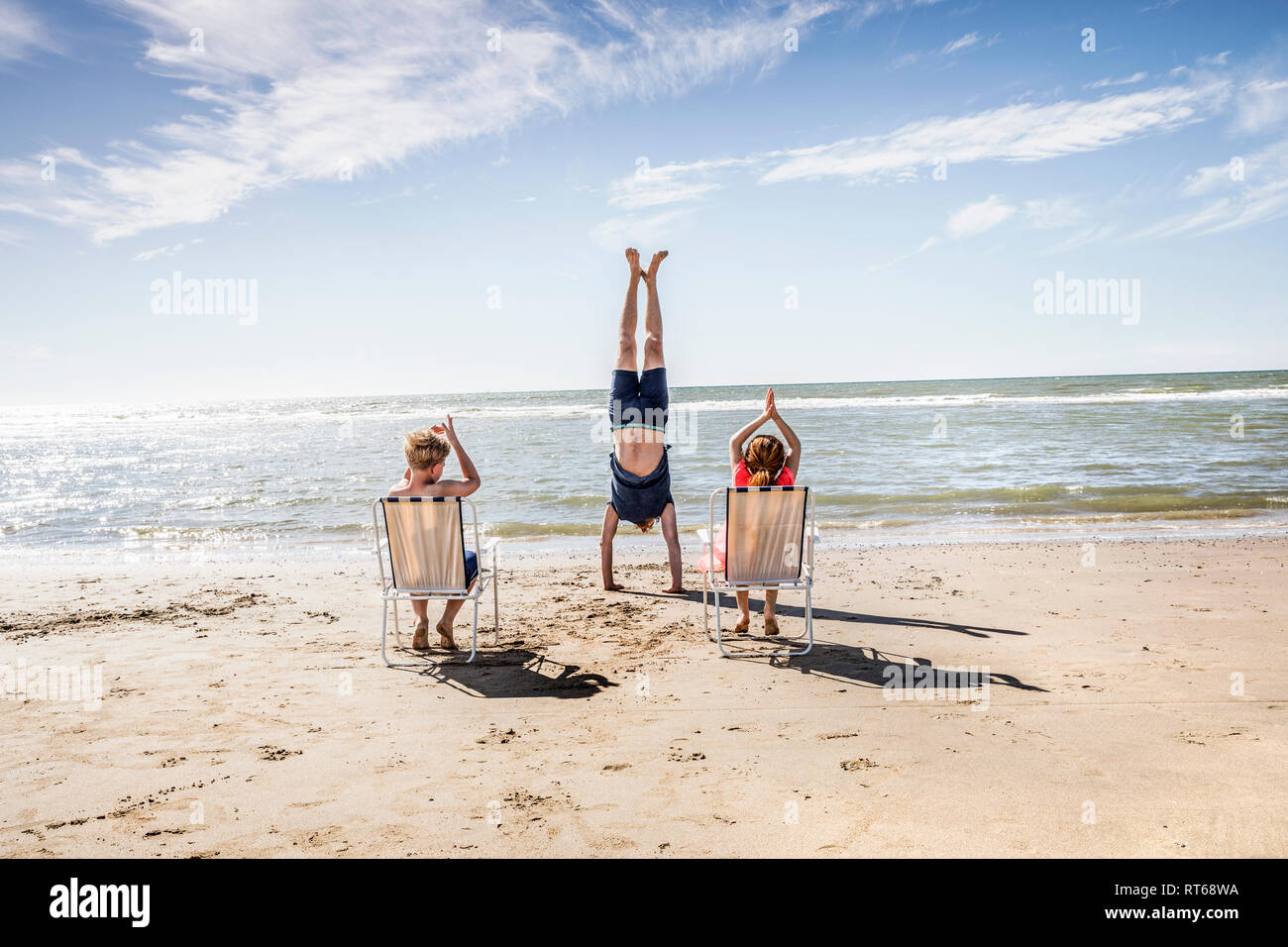 Netherlands, Zandvoort, children clapping hands for father doing a handstand on the beach Stock Photo