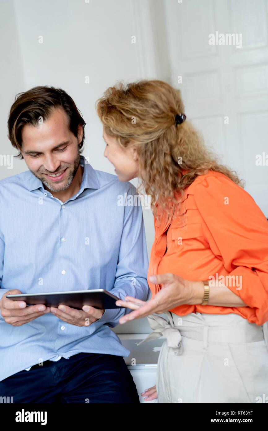 Happy couple working from home, discussing over digital tablet Stock Photo