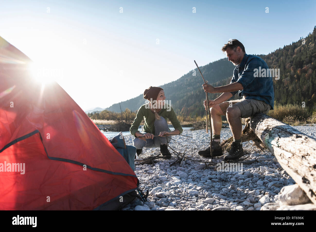 Mature couple camping at riverside, with wood for a camp fire Stock Photo