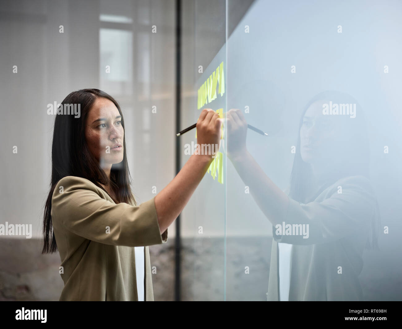 Businesswoman writing on sticky notes at glass pane in office Stock Photo