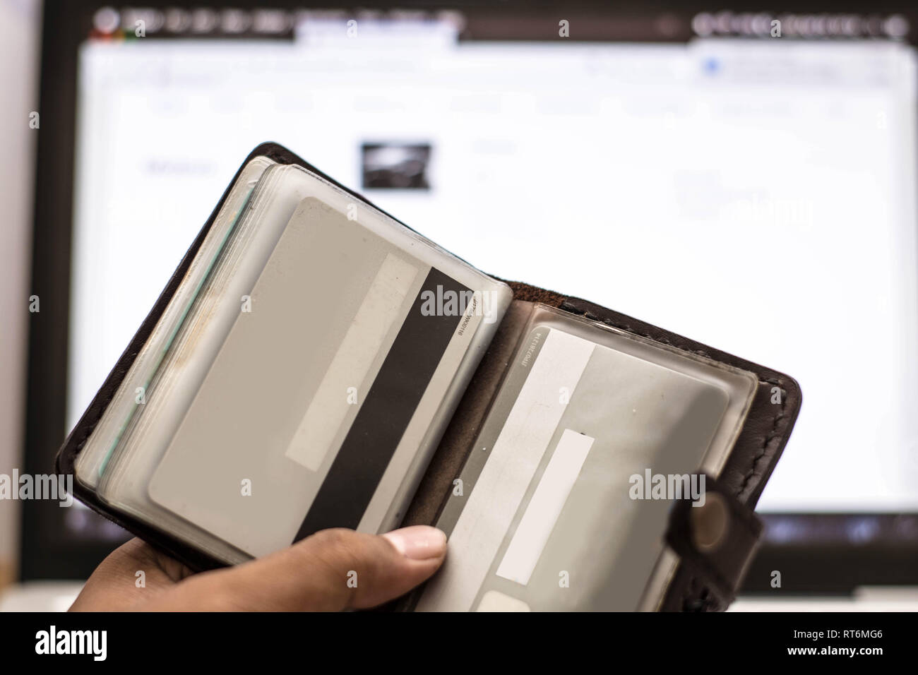 hand holding a card holder with credit card inside in front of computer screen Stock Photo