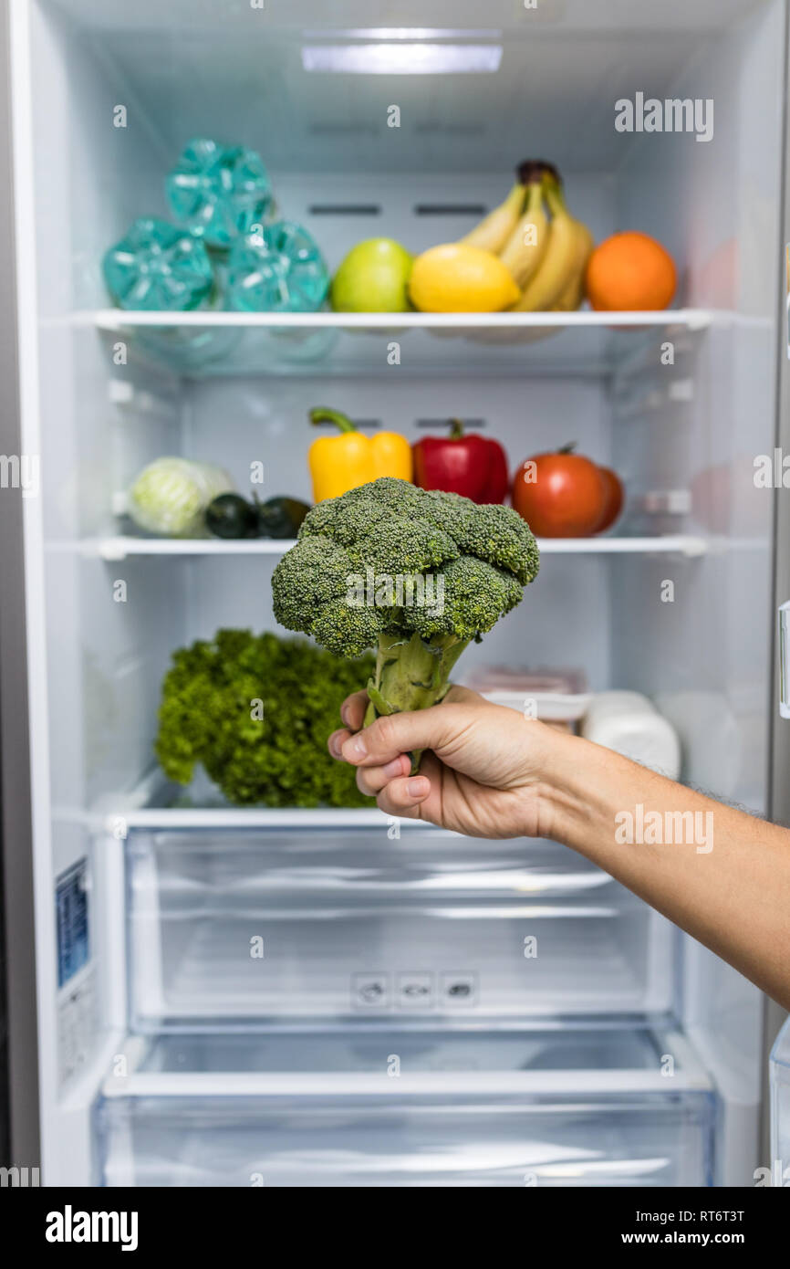 Hands take broccoli from Opened fridge full of fresh colorful fruits