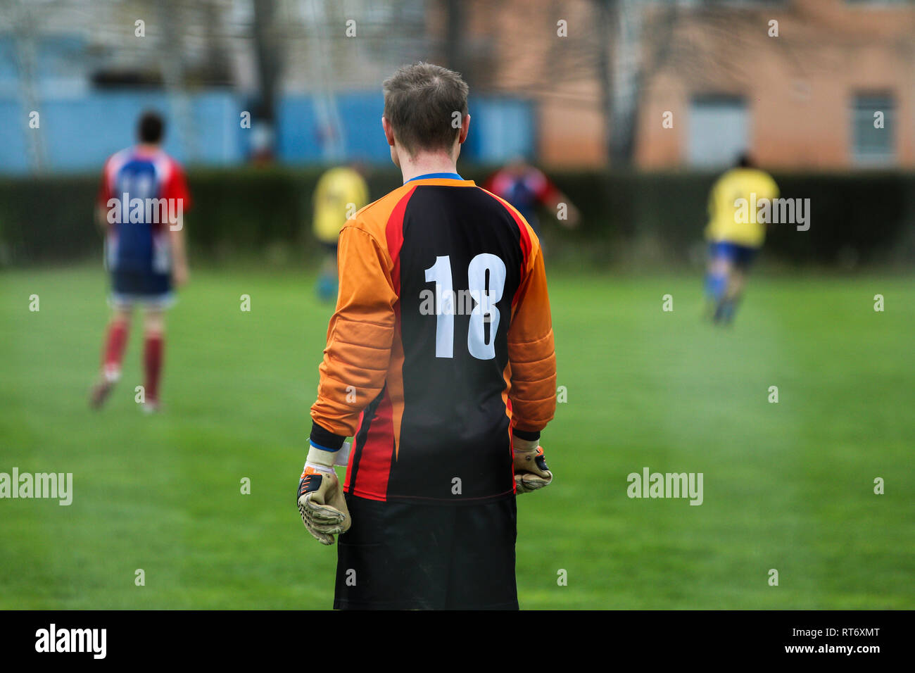 A goalkeeper is standing and looking on his team mates playing the footbal match. Stock Photo