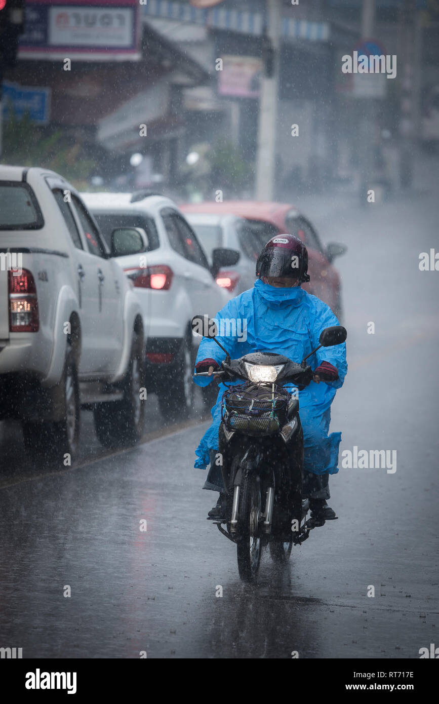 Person riding a moped during a heavy rainstorm in Phuket, Thailand. Stock Photo