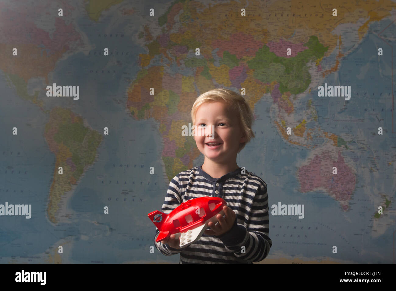 Cute blonde child excitedly holds a red plane in front of a large world map Stock Photo