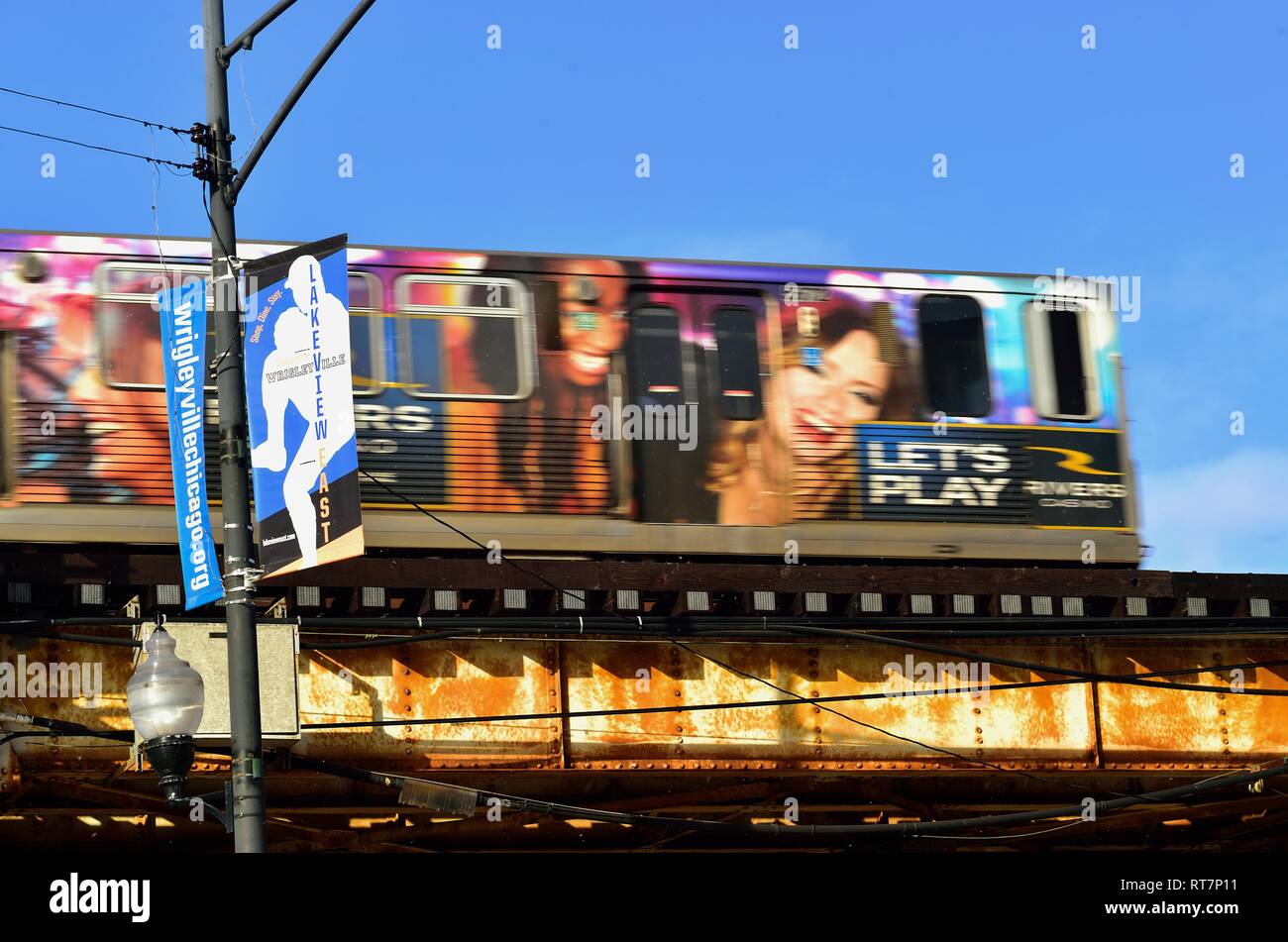 Chicago, Illinois, USA. Light snow falls despite a bright sunny morning as a CTA Red Line L train sporting colorful advertising crosses Clark Street. Stock Photo