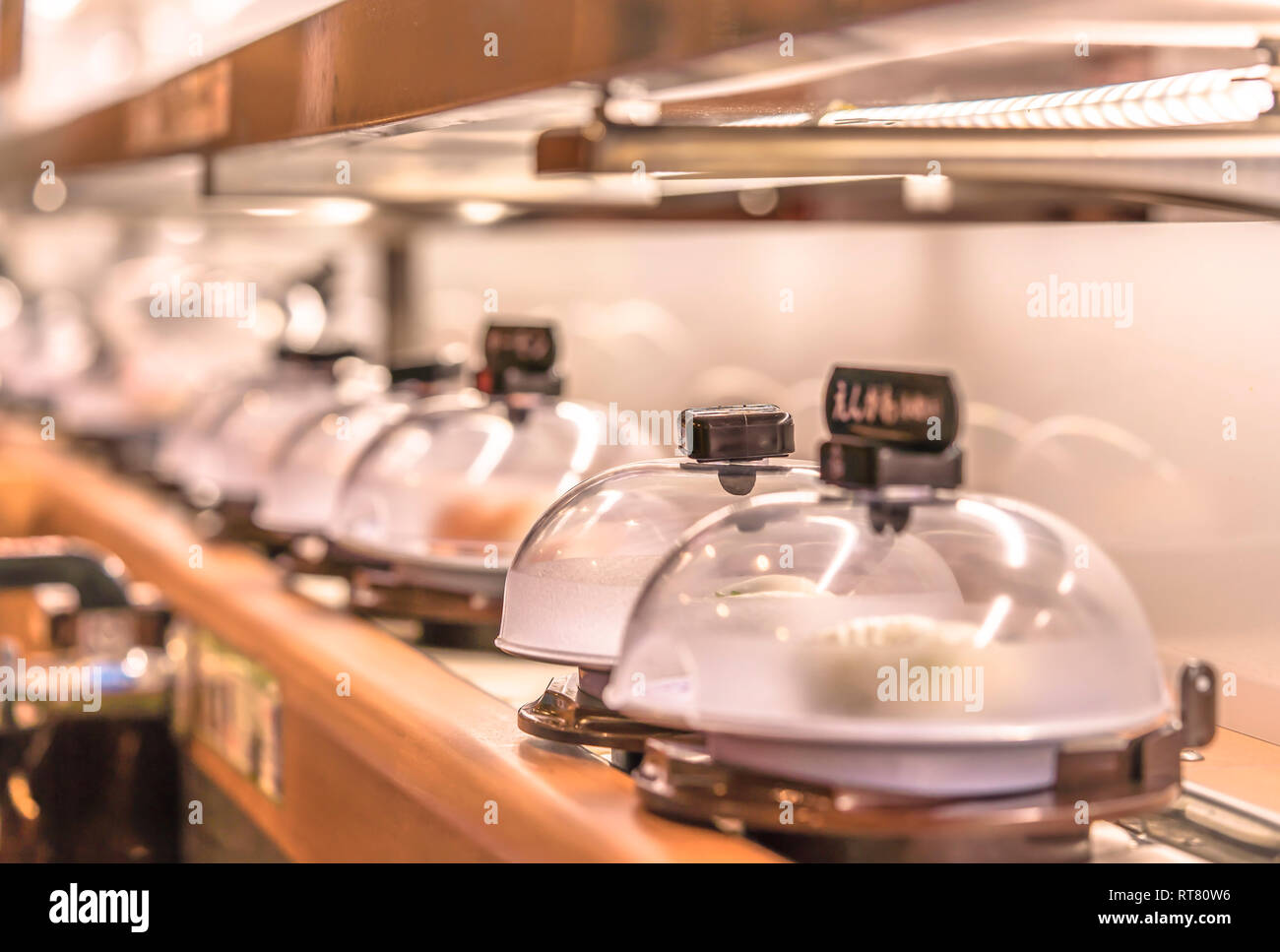 Close-up on Japanese Conveyor belt sushi restaurant where plates with sushi are placed on a rotating rail protected with a clear plastic lid. Stock Photo