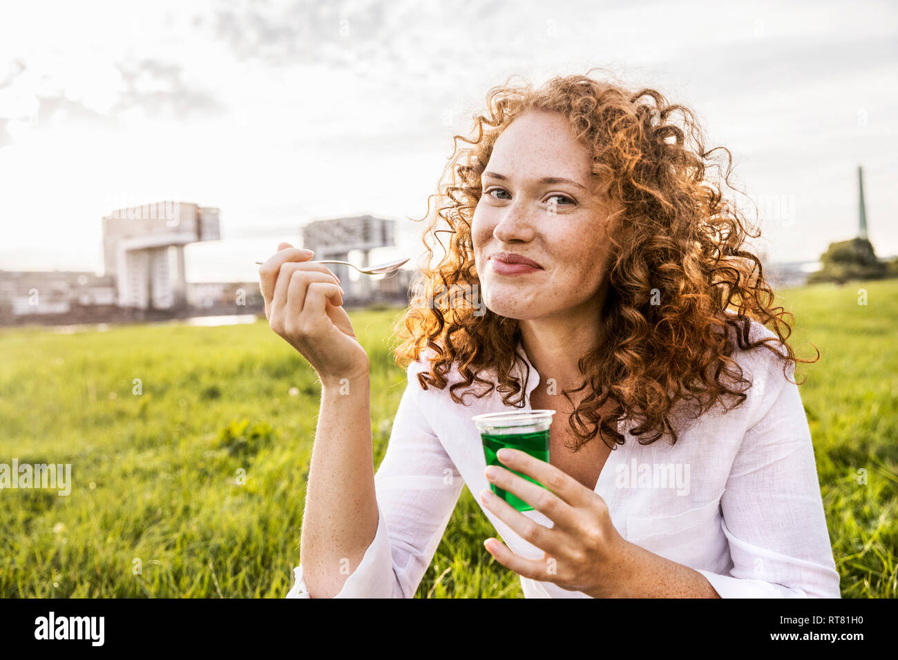 Germany, Cologne, portrait of happy young woman eating jelly on meadow Stock Photo
