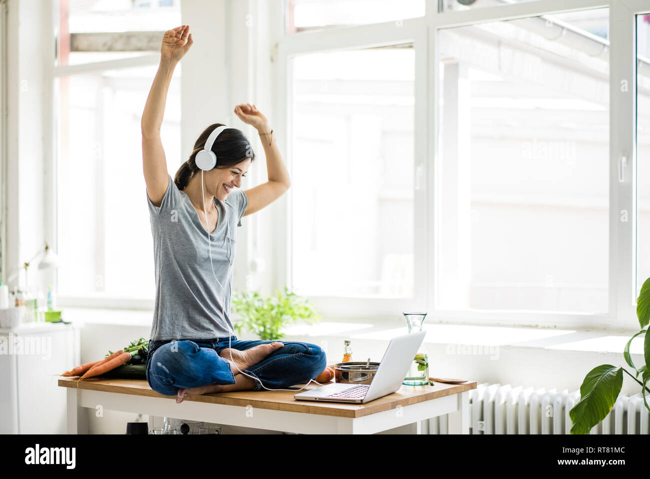 Woman sitting on kitchen table, searching for healthy recipes, using laptop Stock Photo