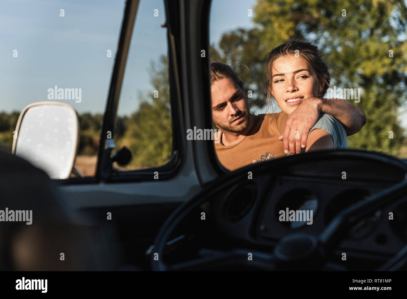 Affectionate couple standing by their camper with arms around Stock Photo