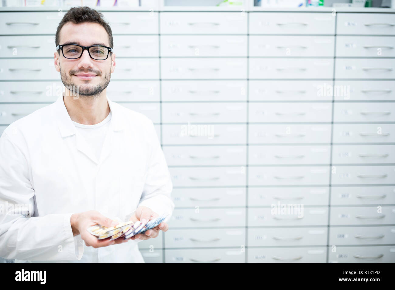 Portrait of smiling pharmacist holding tablet packages at cabinet in pharmacy Stock Photo