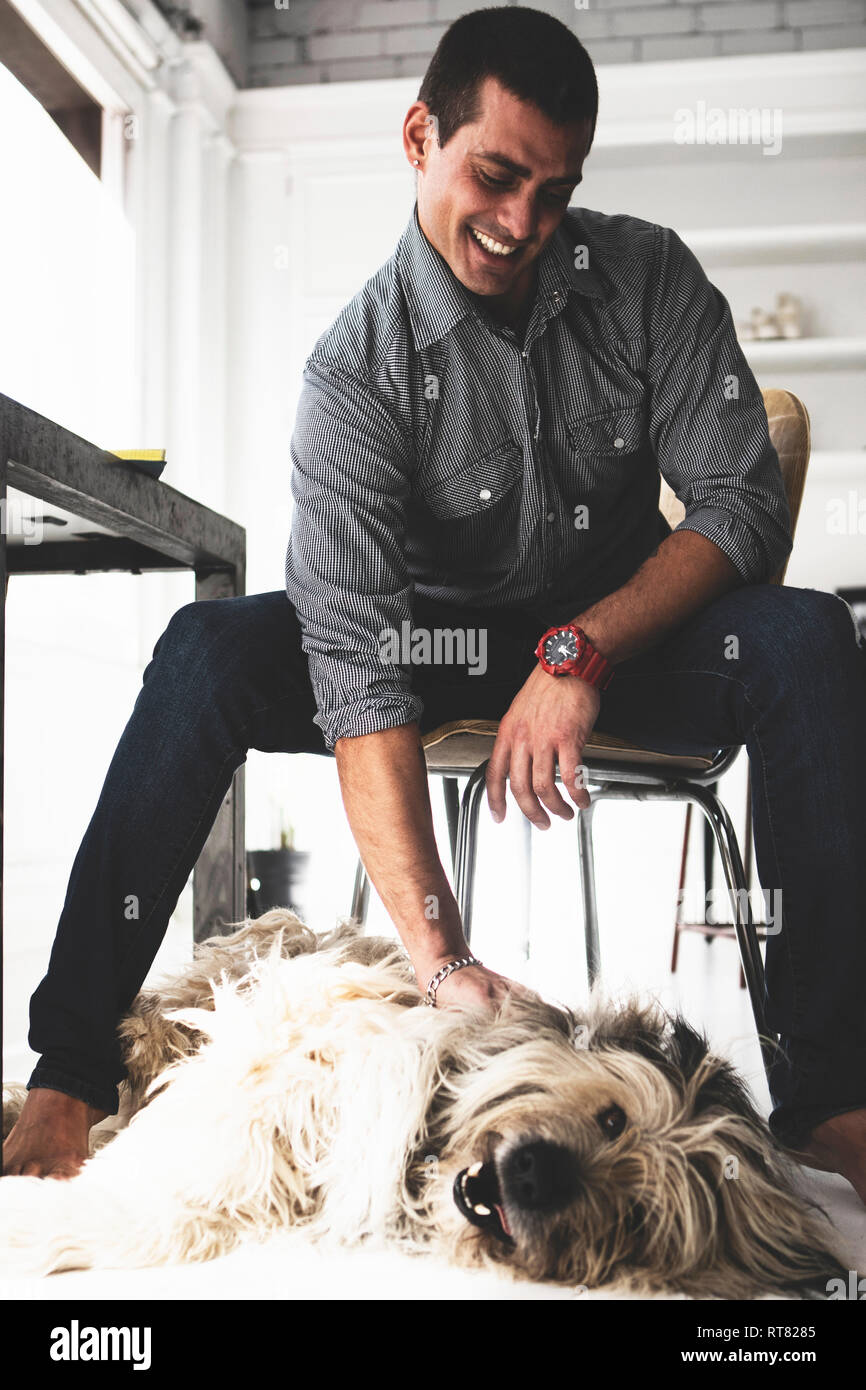 Young man sitting at desk stroking dog Stock Photo