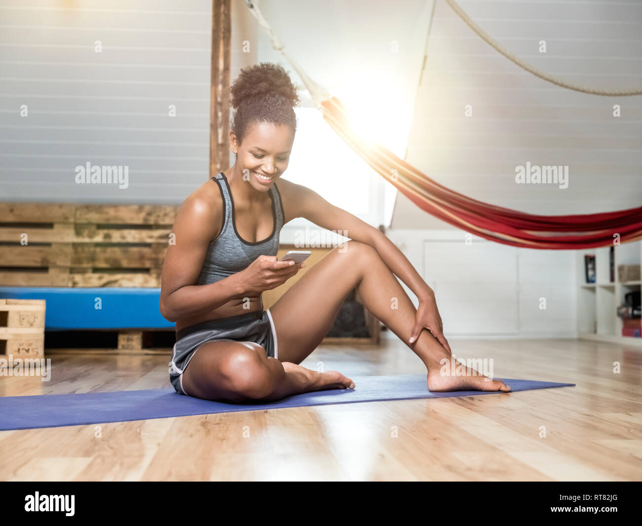 Smiling young woman sitting on yoga mat looking at cell phone Stock Photo