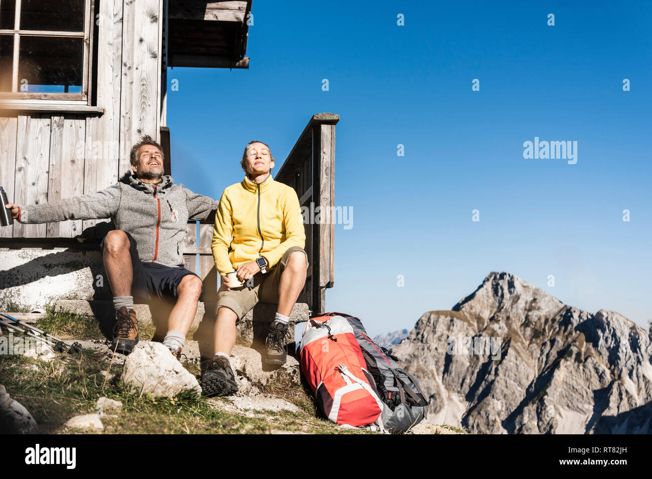 Hiking couple sitting in front of mountain hut, taking a break Stock Photo